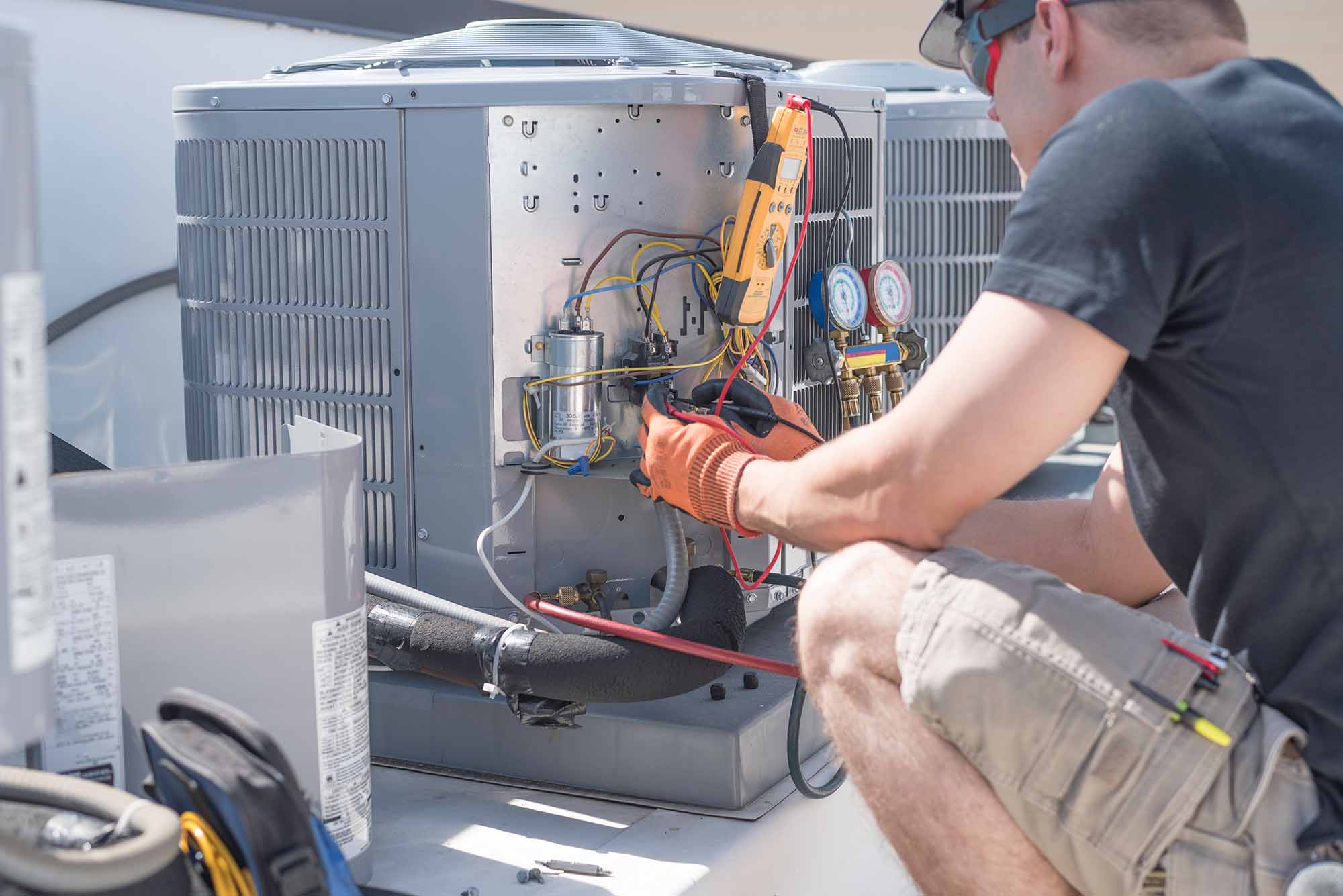 A technician in Johnson City wearing gloves and safety glasses repairs an outdoor HVAC unit, using tools and testing equipment to inspect the wiring and mechanical components.