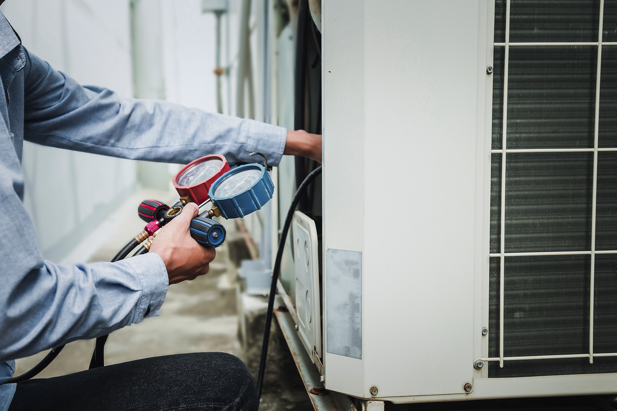 A technician performs AC repair on an outdoor air conditioning unit in Tennessee, using manifold gauges and tools while wearing a light blue shirt.